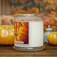 Candle with a pumpkin-themed label on a wooden surface with pumpkins and apples in the background