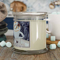 Candle with a 'Marshmellow & Cocoa' label on a wooden surface with marshmallows.