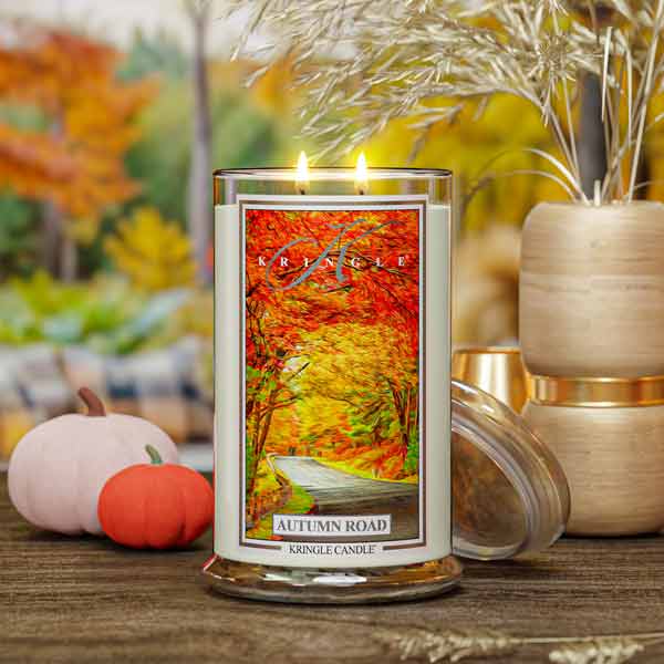 Kringle Candle with 'Autumn Road' design on a wooden surface with blurred autumn-themed background
