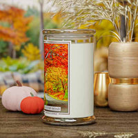 Kringle Candle with 'Autumn Road' design on a wooden surface with blurred autumn-themed background