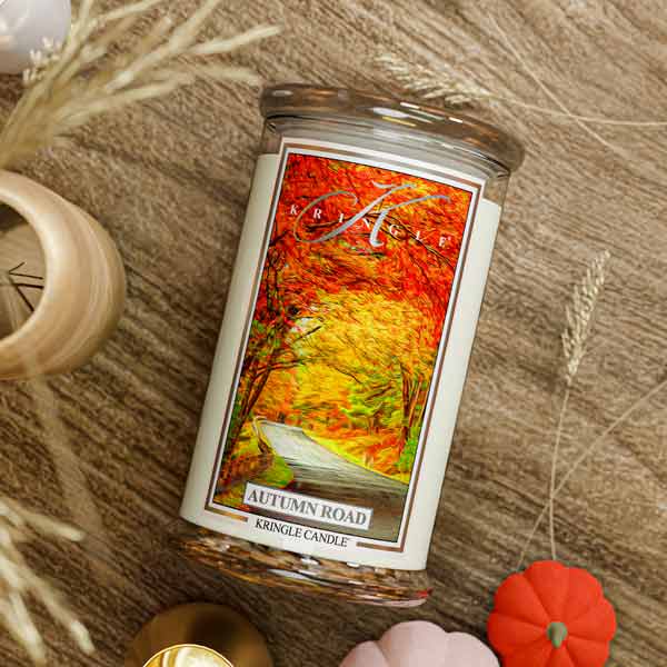 Kringle Candle with 'Autumn Road' design on a wooden surface with blurred autumn-themed background