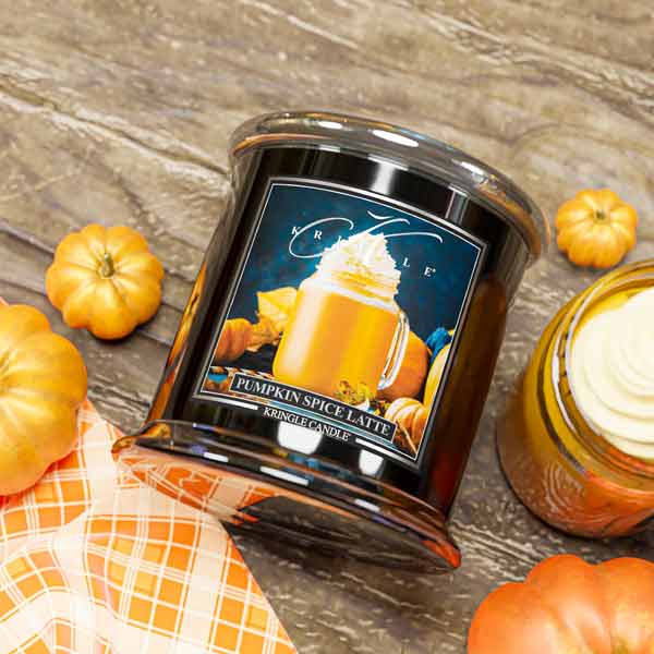 Candle jar labeled 'Pumpkin Spice Latte' surrounded by small pumpkins on a wooden surface