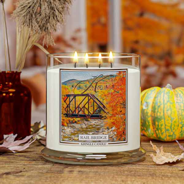 Kringle Candle with 'Rail Bridge' labeled 4-wick candle On a wooden surface with pumpkins and decorative elements.
