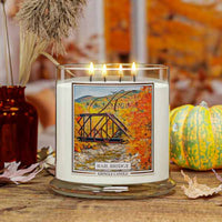 Kringle Candle with 'Rail Bridge' labeled 4-wick candle On a wooden surface with pumpkins and decorative elements.