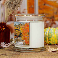 Rail Bridge 4-wick Candle in a glass jar with a decorative label on a wooden surface with pumpkins and leaves.
