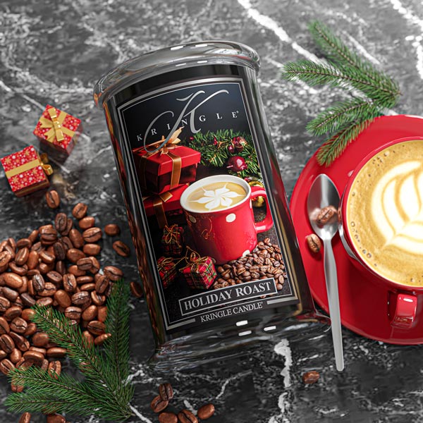 Kringle Candle Holiday Roast candle with coffee beans, a red mug, and Christmas decorations on a dark surface.