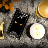 Black cat-themed candle packaging with a lit candle on a textured surface.