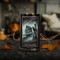 Candle with 'Cabin in the Woods' design on a dark surface with blurred background