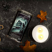 Candle with a label featuring a haunted house design on a dark background with leaves and a spider.