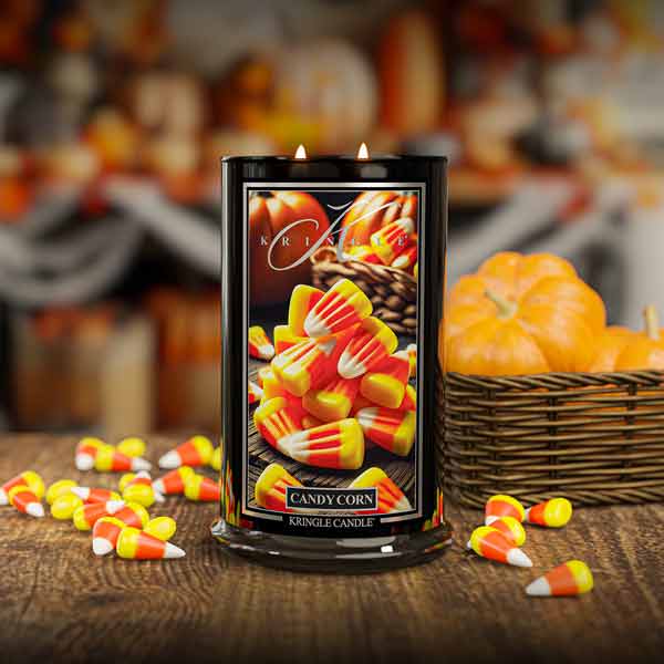 Candle with candy corn design on a wooden surface with pumpkins in the background