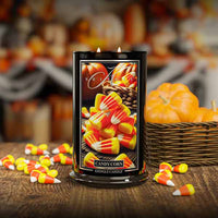 Candle with candy corn design on a wooden surface with pumpkins in the background