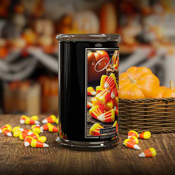 Candle with candy corn design on a wooden table with pumpkins in the background