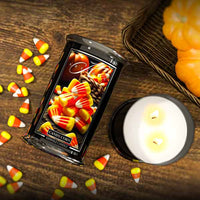 Candy corn-themed candle with packaging on a wooden surface with candy corn and pumpkins.