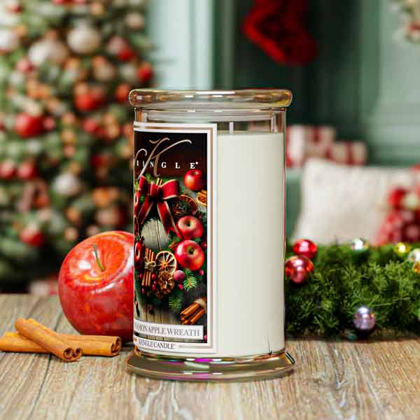 Christmas-themed candle with decorative label in front of a Christmas tree.