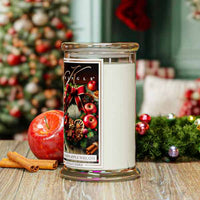 Christmas-themed candle with decorative label in front of a Christmas tree.