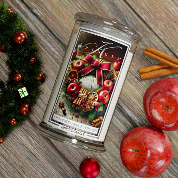 Kringle Candle packaging with Christmas-themed design on a wooden surface with apples and cinnamon sticks.