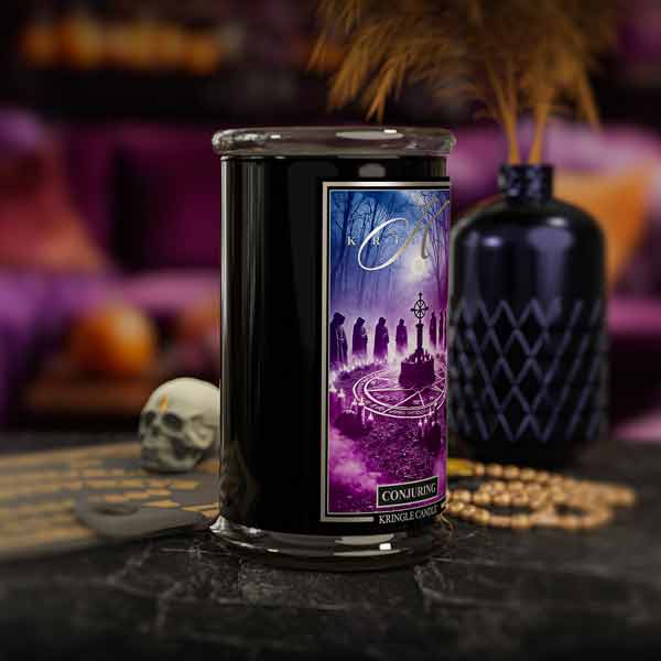 Decorative candle  titled Conjuring with a purple label featuring an illustration of a witch and moon, on a dark surface with a blurred background.