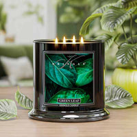 Black Kringle Candle with green leaf design on a wooden surface with plants in the background