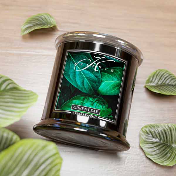 Kringle Candle Green Leaf candle on a wooden surface with decorative leaves.