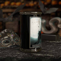 Haunted Hallows Halloween Candle in a black container with a label on a dark surface, surrounded by decorative items.