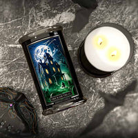 Candle with a decorative label featuring a haunted house design on a textured surface.