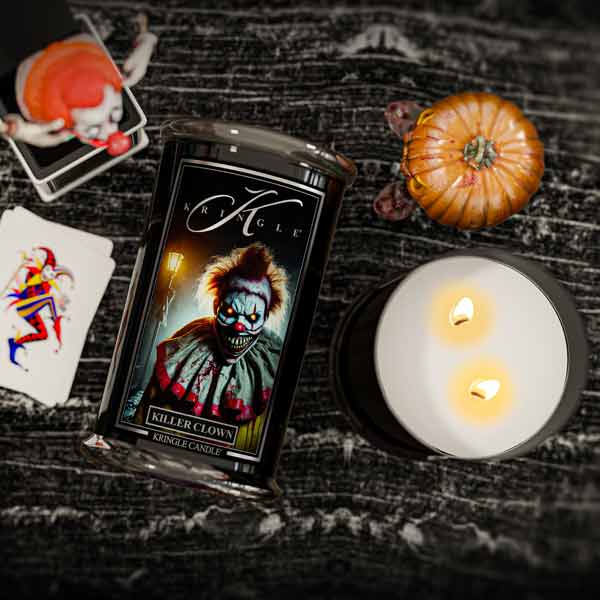 Kringle Candle Killer Clown candle with a lit candle and Halloween-themed items on a dark surface