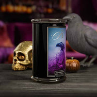 Candle with a decorative label featuring a purple bird design, surrounded by Halloween-themed items like a skull and pumpkins.