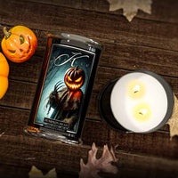 Candle with a pumpkin design and packaging on a wooden surface with pumpkins and leaves.