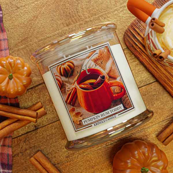 Kringle Candle pumpkin rum toddy candle with pumpkins and cinnamon sticks on a wooden surface