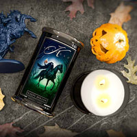 Candle packaging with a horse and moon design next to a lit candle on a dark surface.