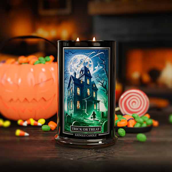 Halloween-themed candle with a haunted house design, surrounded by candy and pumpkins.