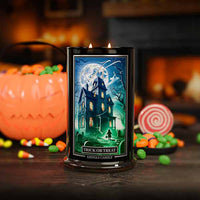 Halloween-themed candle with a haunted house design, surrounded by candy and pumpkins.