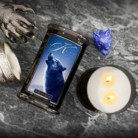 Wiccan candle with wolf design on a dark surface with a lit candle and wolf figurine.