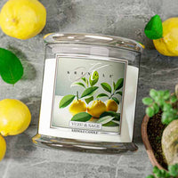 Kringle Candle with Yuzu & Sage flavor surrounded by lemons and a plant on a gray surface