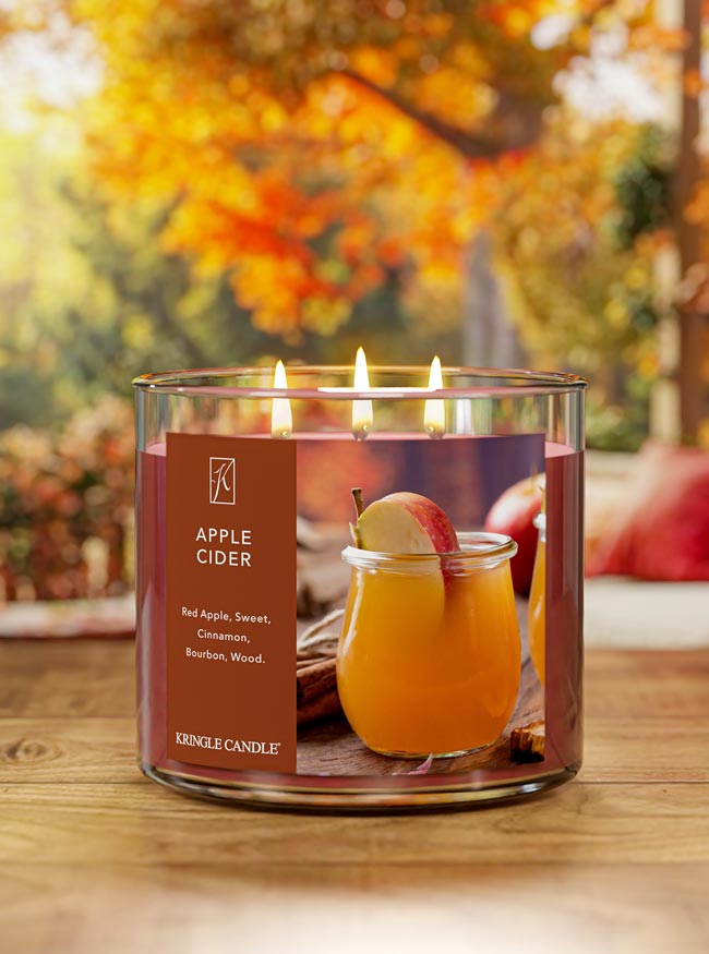 Kringle Candle with 'Apple Cider' label on a wooden surface with blurred autumn background