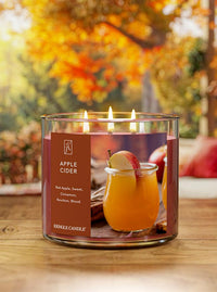 Kringle Candle with 'Apple Cider' label on a wooden surface with blurred autumn background