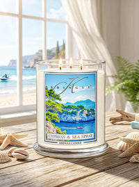 Kringle Candle with 'Cypress & Sea Spray' scent on a table by a window with a view of the ocean.