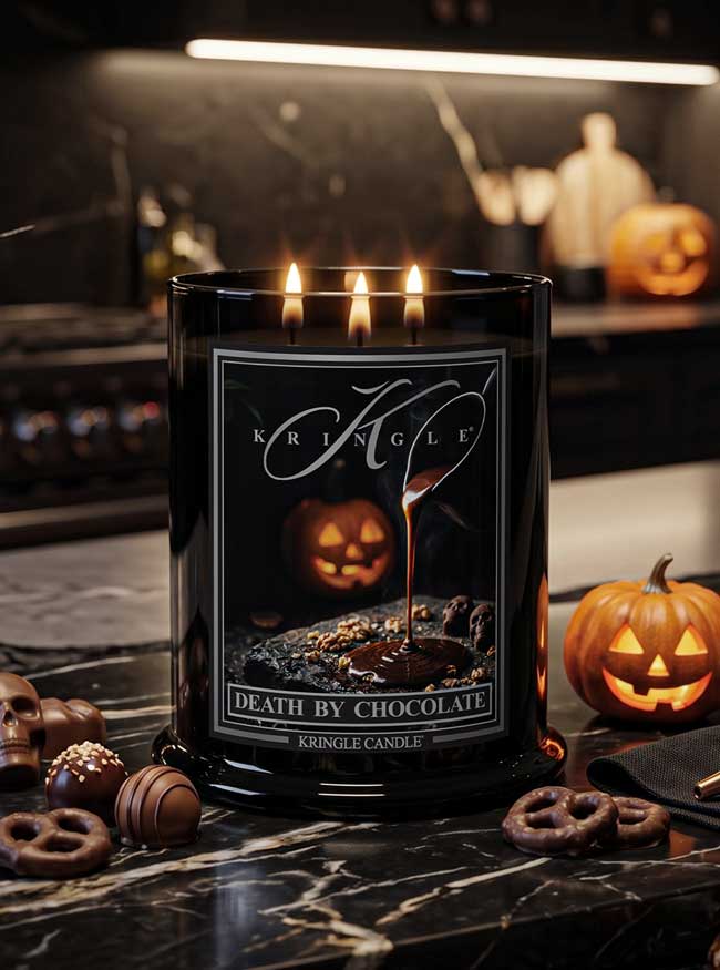 A black glass jar candle with three lit wicks and a Halloween-themed label reading 'Kringle' and 'Death by Chocolate,' placed on a dark marble surface with chocolate pieces, pretzels, and jack-o'-lanterns around it.