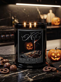 A black glass jar candle with three lit wicks and a Halloween-themed label reading 'Kringle' and 'Death by Chocolate,' placed on a dark marble surface with chocolate pieces, pretzels, and jack-o'-lanterns around it.