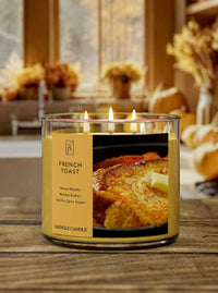 Kringle Candle lit French Toast scented candle with a picture of French toast on the label and candle sets on a wood table with a fall-themed background