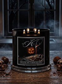 A black glass jar candle with three lit wicks sits on a rustic wooden table. The front label reads 'KRINGLE' and 'DEATH BY CHOCOLATE' with a pumpkin and chocolate imagery.