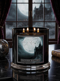 A black three-wick candle labeled 'Haunted Hallows' by Kringle Candle, set on a dark reflective table with a gothic window, moon, and castle visible in the background.