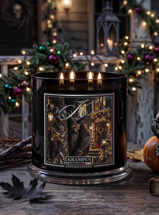 A large black glass jar candle with four lit wicks sits on a rustic wooden table. The front label reads 'Krampus Kringle Candle' and shows a dark festive illustration.