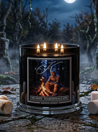 A large black candle jar with four lit wicks sits on a stone surface in a spooky forest setting at night. The front label reads 'Kingle Candle' and 'Mummy Marshmallow,' with an illustration of a mummy by a campfire.