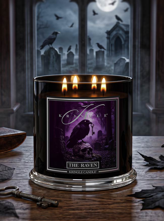 A black glass jar candle with four lit wicks and a purple gothic label reading 'The Raven' and 'Kringle Candle,' placed on a wooden table with a spooky graveyard scene in the background.