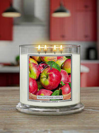 Kringle Candle lit Macintosh Apple scented candle with apple illustration on a kitchen counter with kitchen cupboards in the background.