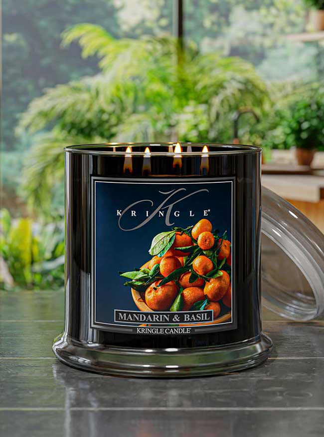 Kringle Candle with Mandarin & Basil fragrance on a reflective surface with a garden background