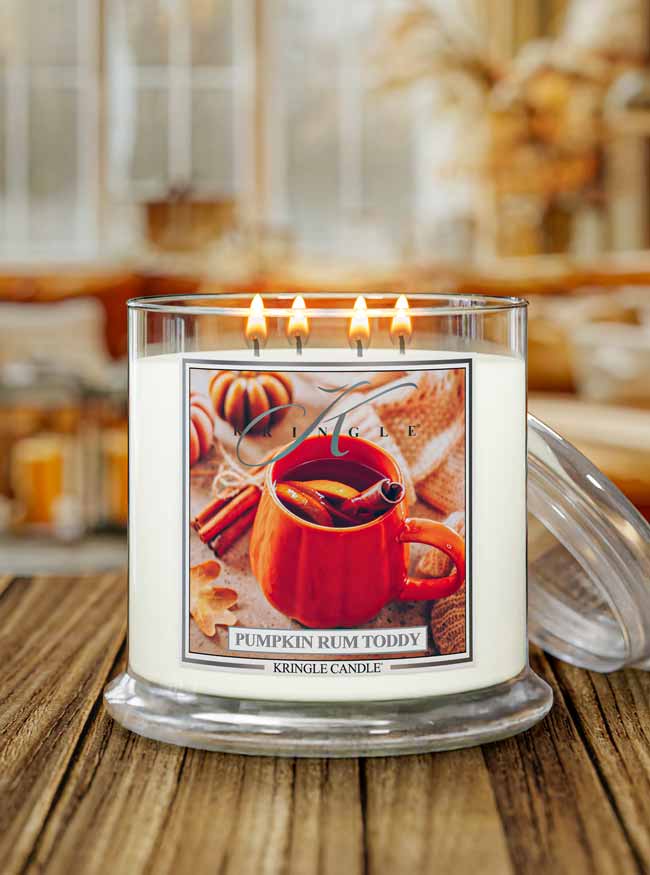 Kringle Candle Pumpkin Rum Toddy 4-wick lit candle with a label with a fall background