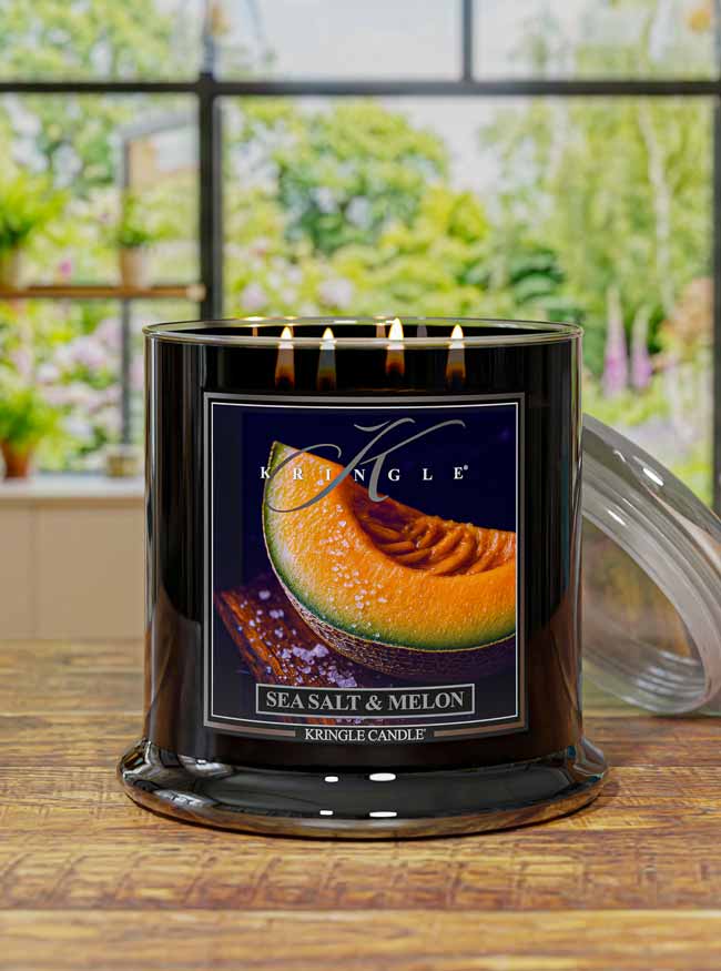 Kringle Candle with 'Sea Salt & Melon' label design on a wooden surface with a blurred outdoor background