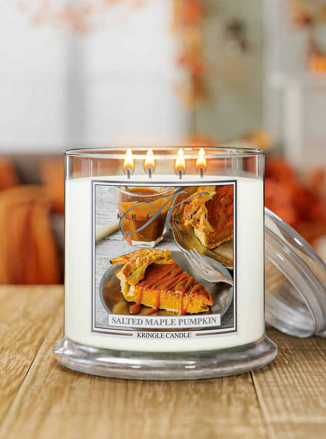 A three-wick Kregolt Candle in a clear glass jar sits on a wooden table with its lid beside it. The candle label features a photo of a slice of salted maple pumpkin pie, with the text 'SALTED MAPLE PUMPKIN' and 'KREGOLT CANDLE' below.